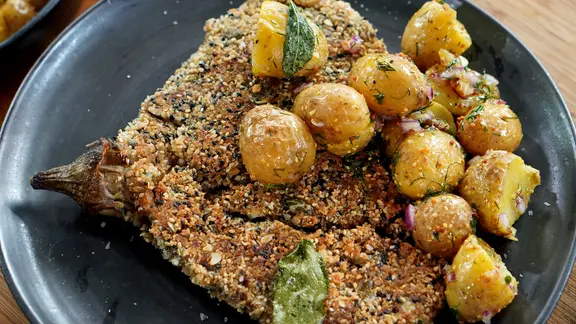 Knusperschnitzel aus Auberginen mit Kartoffeln auf einem Teller serviert.