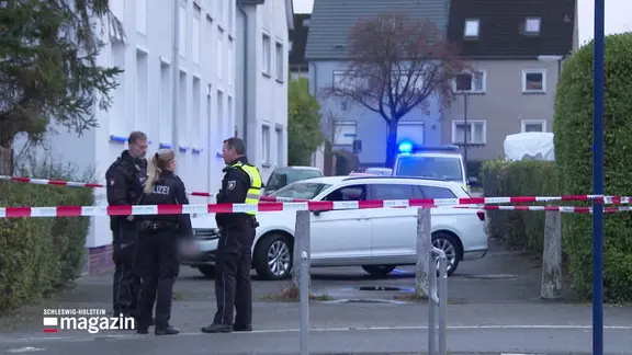 Drei Polizisten stehen hinter einem Sperrband.