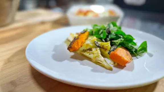 Gebackener Chicorée mit Ziegenkäse, Quitte, Kürbis und Feldsalat auf einem weißen Teller angerichtet