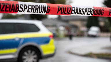 Vor einem Einsatzfahrzeug der Polizei ist ein Flatterband mit der Aufschrift "Polizeiabsperrung" zu sehen.