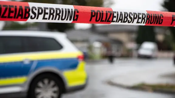 Vor einem Einsatzfahrzeug der Polizei ist ein Flatterband mit der Aufschrift "Polizeiabsperrung" zu sehen.