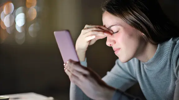 Eine Frau schaut auf ihr Handy und kneift dabei die Augen zu.