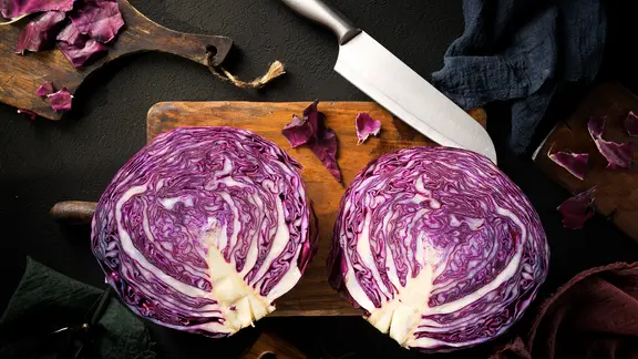 Rotkohl: Rotkraut-Kohlkopf in zwei Hälften auf Schneidebrett mit Messer