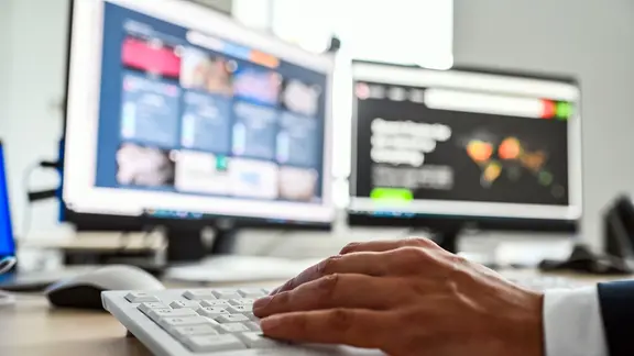 Auf zwei Computerbildschirmen sind Fotos und Videos zu sehen.