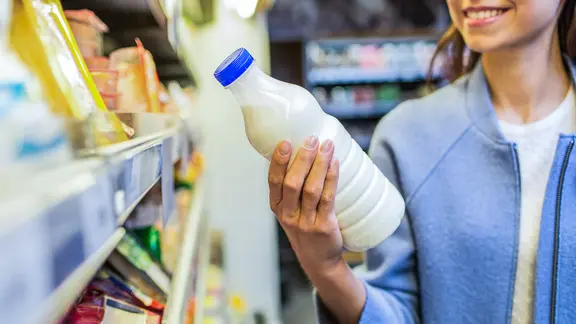 Eine junge Frau betrachtet eine Milchflasche im Supermarkt.