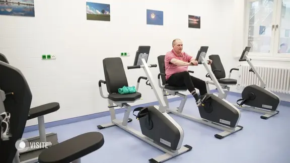 Ein Mann sitzt in einem Fitnessraum auf einem Fahrrad und trainiert.