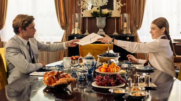 Ein junger Mann überreicht einer jungen Frau an einem festlich gedeckten Tisch Dokumente.