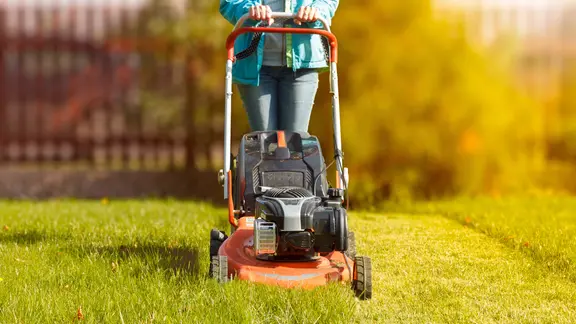 Eine Frau schiebt einen Rasenmäher auf einer Rasenfläche vor sich her.