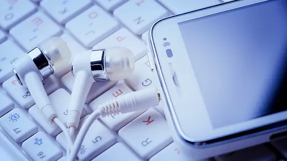 Kopfhörer mit Smartphone liegen auf einer Computertastatur.