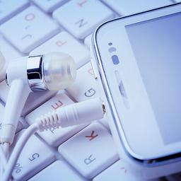 Kopfhörer mit Smartphone liegen auf einer Computertastatur.