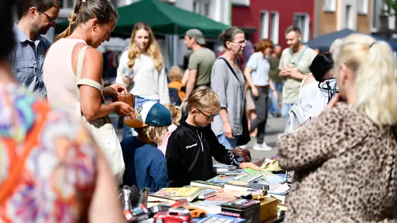 Kinder und Erwachsene sind auf einem Flohmarkt bei Sommerwetter unterwegs.