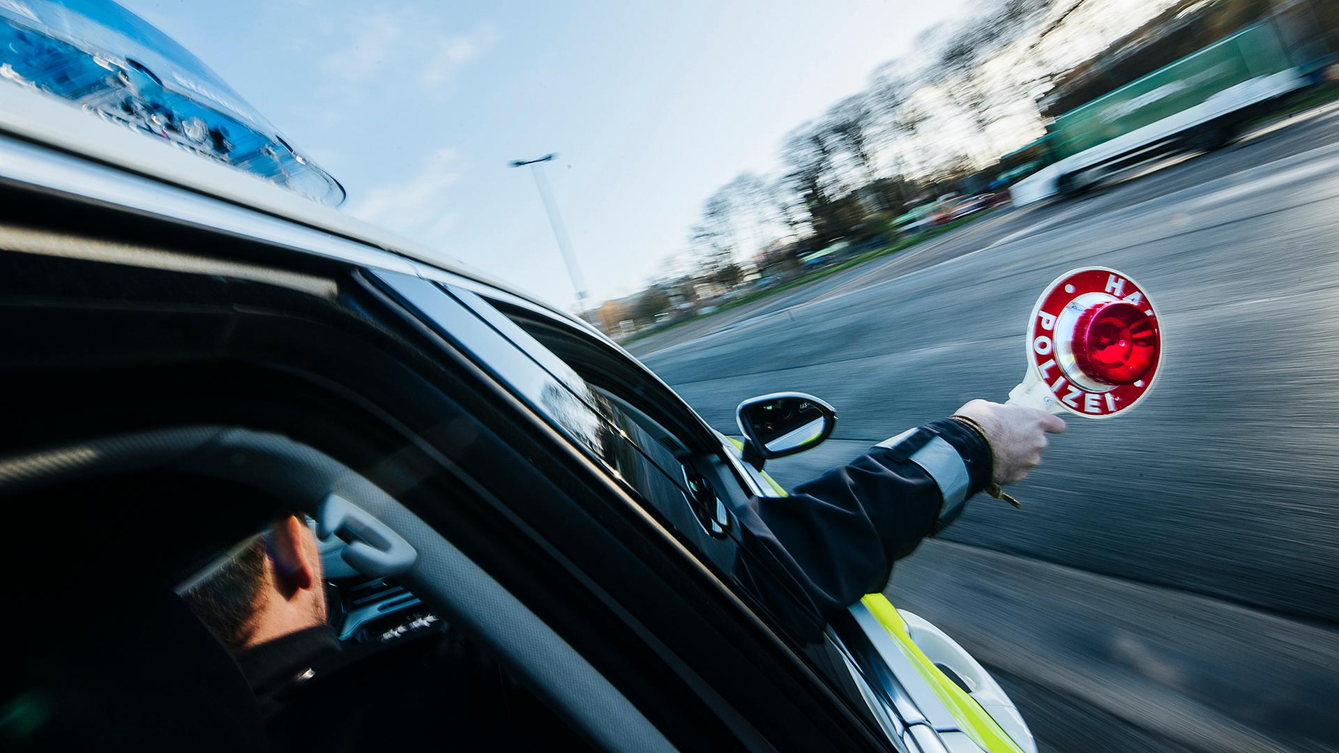 Ein Polizist hält eine rote Polizeikelle aus dem Beifahrerfenster eines Streifenwagens heraus. | NDR, Julius Matuschik