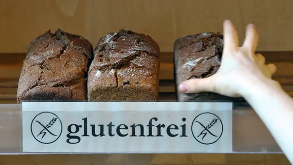 Eine Hand greift in einem Naturkostladen nach einem glutenfreien Brot. | Peter Endig / dpa, Peter Endig Eine Hand greift in einem Naturkostladen nach einem glutenfreien Brot.