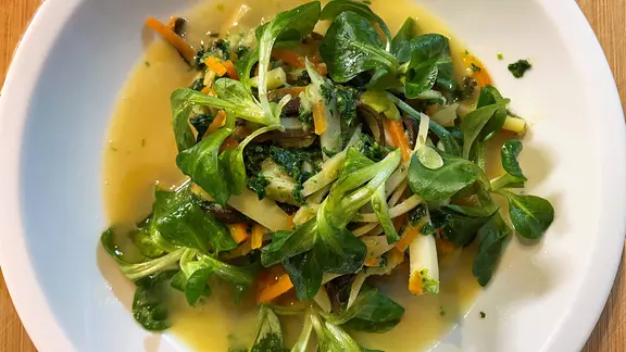 Wurzelgemüse mit Spaghettialgen, Grünkohl und Feldsalat auf einem Teller serviert.