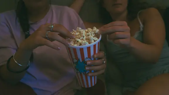 Zwei Frauen sitzen auf dem Sofa und teilen sich eine Tüte Popkorn.