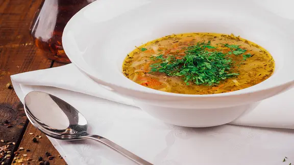 Ein tiefer Teller mit einer Gemüsesuppe, daneben ein Löffel.