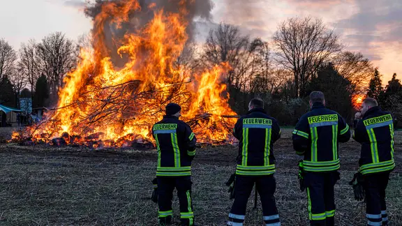 Vor einem Osterfeuer stehen vier Feuerwehrmänner.
