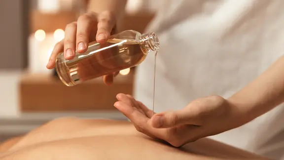 Ein Masseur gießt sich Öl aus einer kleinen Flasche in die Hand. | IMAGO / Pond5 Images Ein Masseur gießt sich Öl aus einer kleinen Flasche in die Hand.