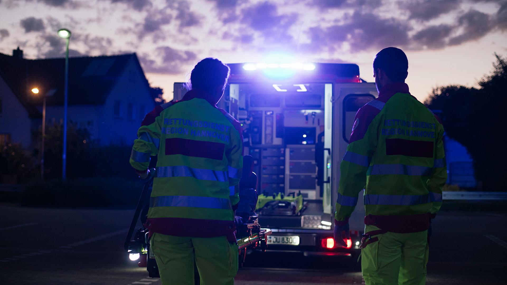 Zwei Sanitäter laden bei Dunkelheit die Trage in den Rettungswagen ein. | NDR, Julius Matuschik