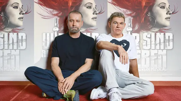 Ulf Leo Sommer und Peter Plate sitzen vor einem Plakat