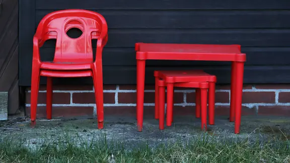 An einer Hauswand stapeln sich rote Kindermöbel, Stühle und Tische.