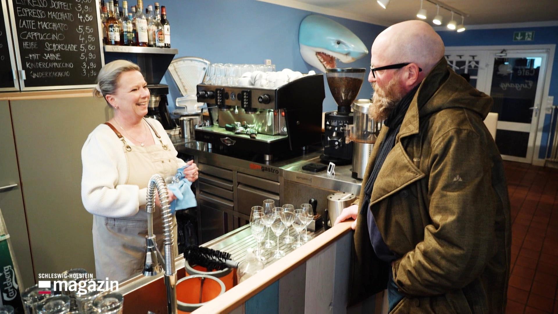 Eine Frau steht in einer Bar hinter dem Tresen und trocknet Gläser ab, lächelnd spricht sie mit einem Mann. | Screenshot