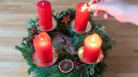 Anzünden eines Adventskranzes, drei Kerzen brennen.