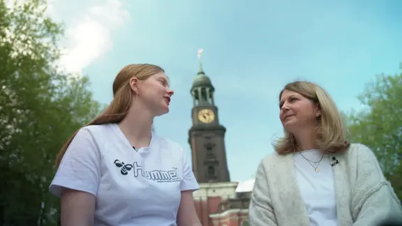 Zwei Frauen unterhalten sich. Im Hintergrund ist der Hamburger Michel zu sehen.