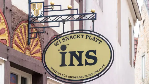 An einem Altstadthaus in Bremen hängt ein Schild mit der Aufschrift "INS - Wi snackt Platt - Institut für niederdeutsche Sprache".