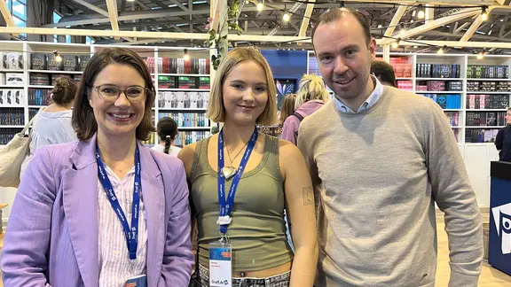 Maria Meibohm, Emma Grunwald und Frederick Wrensch von der Graff-Buchhandlung. | NDR, Julia Hercka Drei Menschen vor Bücherregalen in einem Flur lächeln in die Kamera.