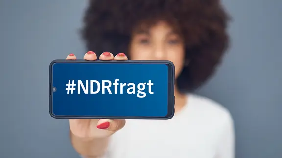 Eine Frau hält ein Smarthphone in die Kamera, auf dem Display steht "#NDRfragt"
