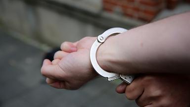 Ein Polizist sichert Hand eines Mannes mit Handschellen.