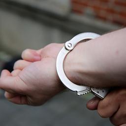 Ein Polizist sichert Hand eines Mannes mit Handschellen.