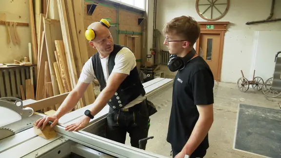 Ein Handwerker und sein Praktikant stehen in der Holzwerkstatt