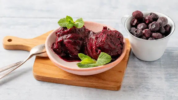 Ein Schälchen mit einem Blaubeersorbet, daneben frische Blaubeeren.