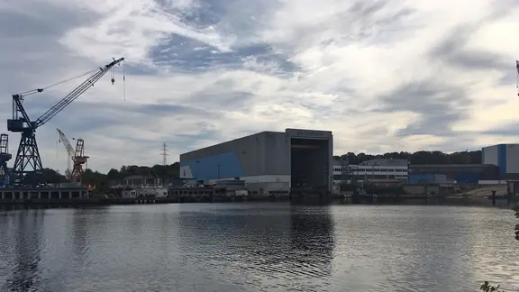 Das Dockgebäude der Werft Nobiskrug in Rendsburg steht vor leicht bewölktem Himmel.