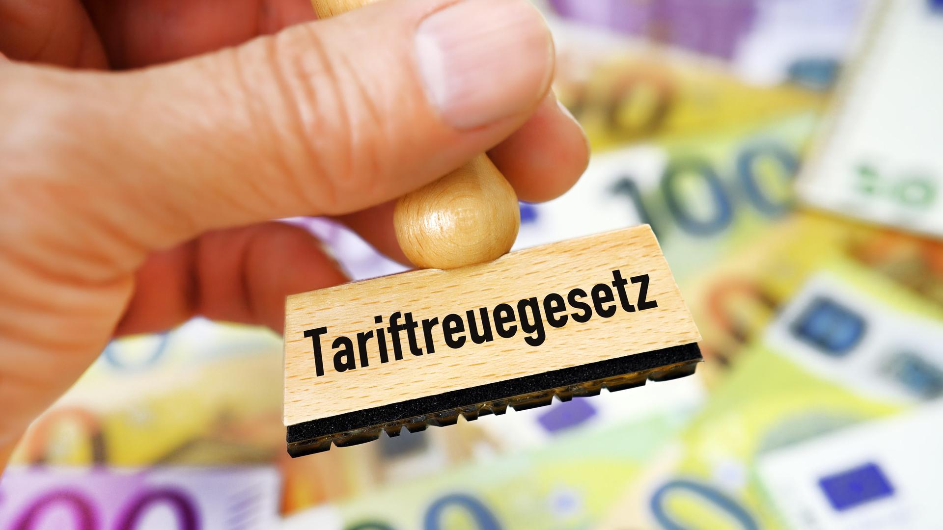 Hand hält Stempel mit Aufschrift Tariftreuegesetz vor Geldscheinen, Fotomontage | CHROMORANGE | Christian Ohde