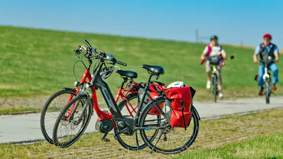Fahrräder und Radfahrer auf einem Radweg hinter dem Deich in Carolinensiel