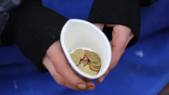 Ein Obdachloser hält einen Pappbecher mit Kleingeld in der Hand.