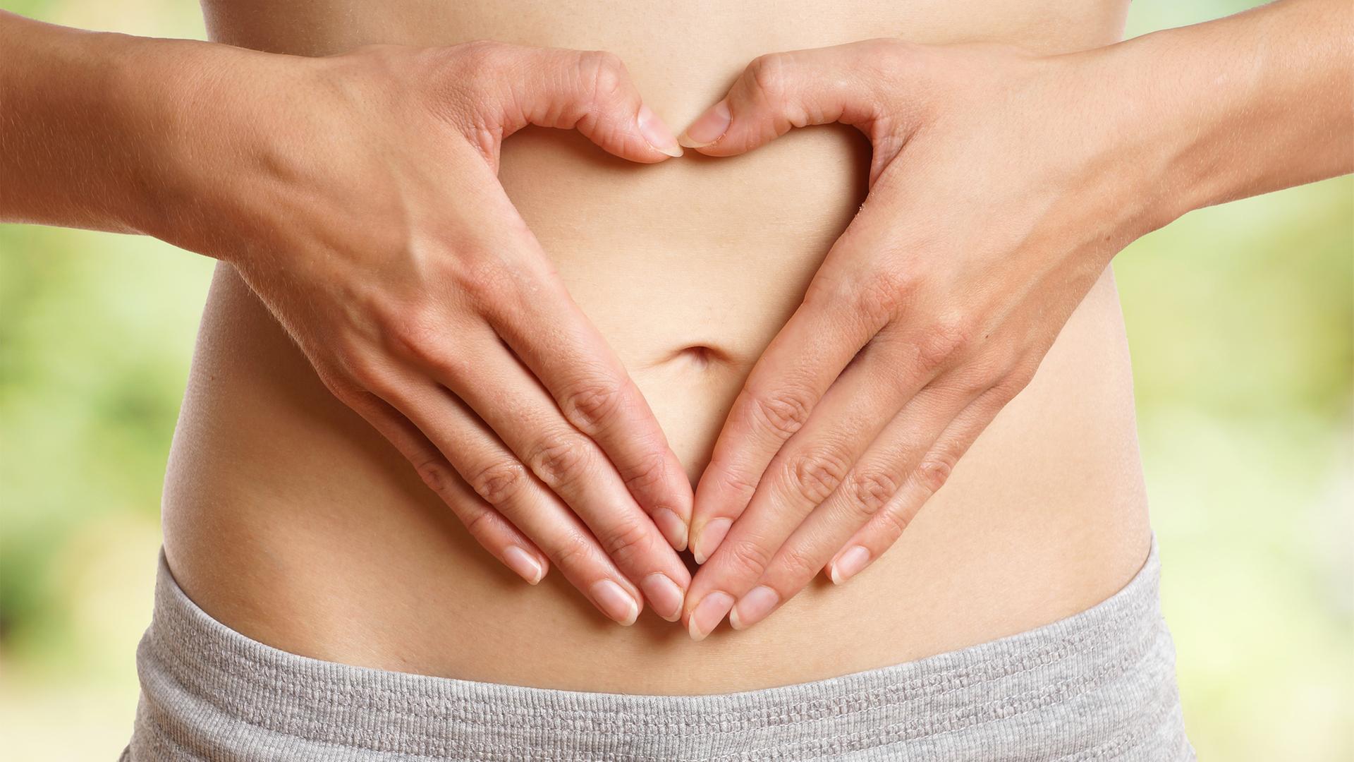 Eine Frau mit einem grauen Slip formt mit ihren Händen ein Herz und hält sie schützend vor ihren nackten Bauch. | fotolia.com, underdogstudios