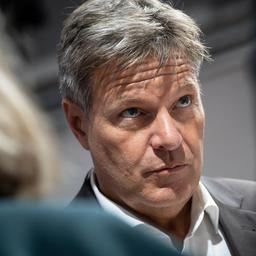 Wirtschaftsminister Robert Habeck steht zwischen zwei Menschen, die von hinten zu sehen sind, und hört ihnen zu.