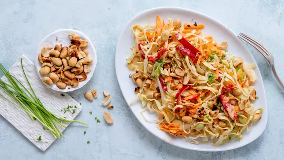 Ein Teller mit einem Spitzkohlsalat, daneben ein Schälchen mit Erdnüssen.
