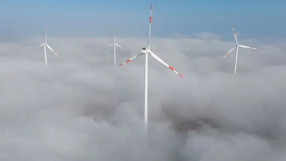 Windräder ragen aus dem Nebel hervor.