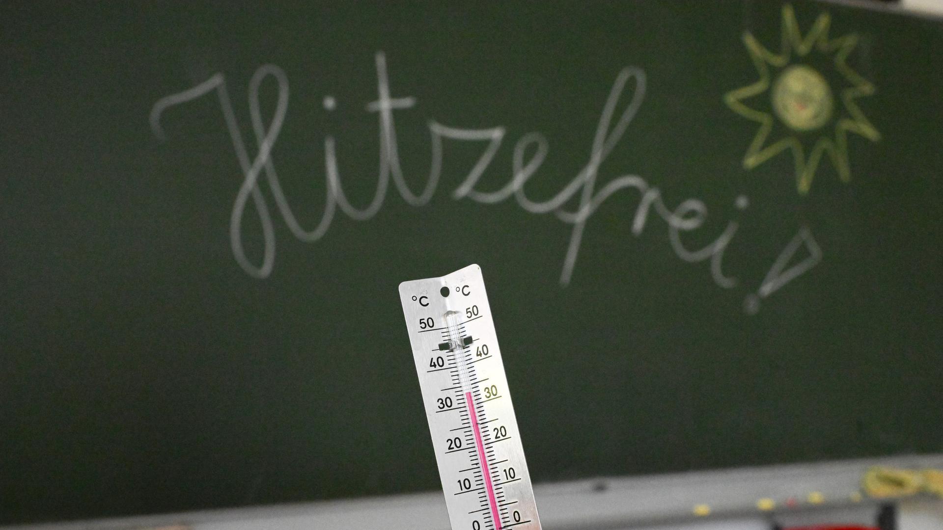 Ein Thermometer vor einer Schultafel zeigt 33 Grad. An der Tafel steht mit Kreide das Wort Hitzefrei geschrieben. | picture alliance/Bernd Weißbrod