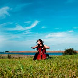 Eine Cellistin sitzt auf einer grünen Wiese vor blauem Himmel (Imagebild der Festspiele MV).
