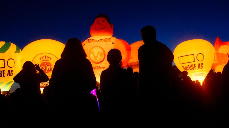 "Night Glow": Die beleuchteten Ballone locken jedes Jahr viele Zuschauer auf das Nordmarksportfeld. | Landeshauptstadt Kiel, Bodo Quante Heißluftballons im Abendlicht leuchten durch das in sie geblasene Feuer