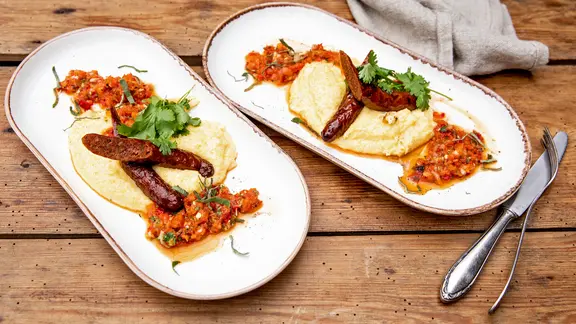 Salbei-Polenta mit Paprika-Relish und Merguez auf einem Teller serviert.