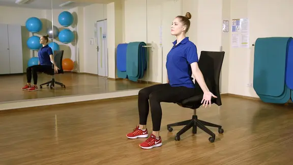 Svea Köhlmoos sitzt auf einem Drehstuhl und zeigt eine Übung.