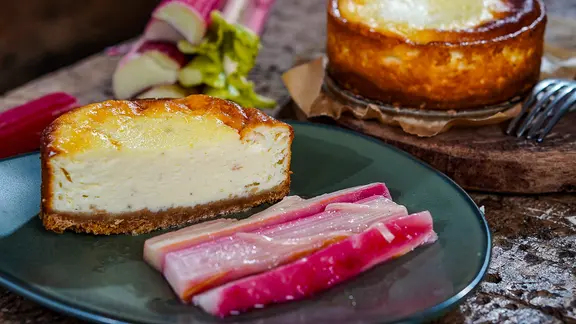 Cheesecake mit pochiertem Rhabarber auf einem Teller serviert