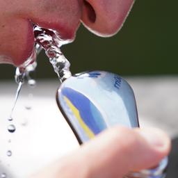 Ein Mann in Hamburg trinkt Wasser aus einem Wasserspender.